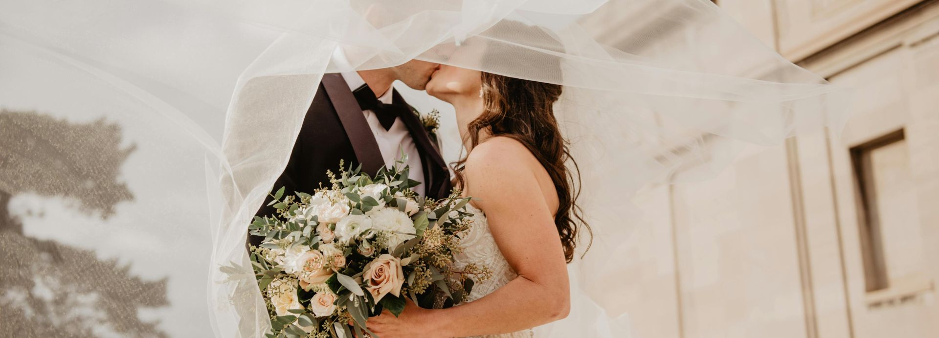 Bride and groom share a tender kiss under a veil, showcasing love and romance on their special day.