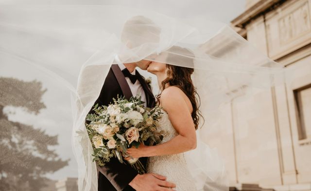 Bride and groom share a tender kiss under a veil, showcasing love and romance on their special day.